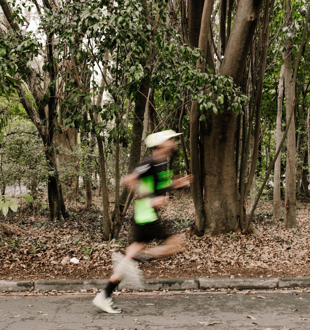 Felipe correndo de lado, em movimento borrado, entre as árvores do Ibirapuera